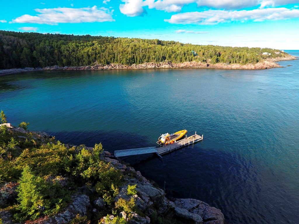 Vue aérienne de notre anse aux Escoumins : le quai, un zodiac et la forêt au bord du fleuve